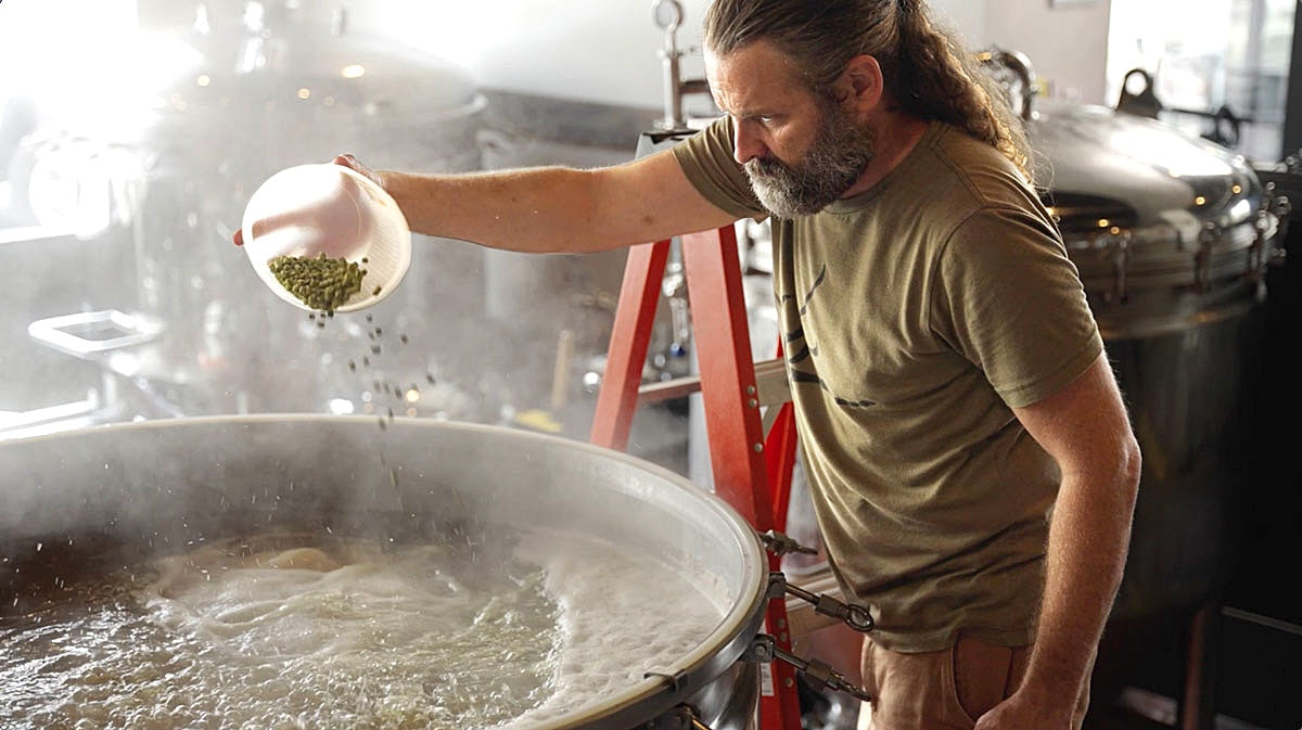 Man adding hops to a large kettle in a brewery setting